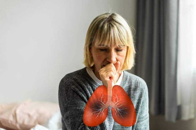 A woman coughs into her hand, with an illustration of inflamed lungs, indicating respiratory illness.