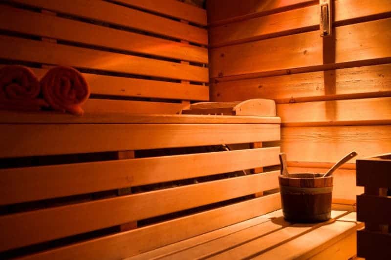 Wooden sauna interior with benches and a bucket, warmly lit for relaxation.