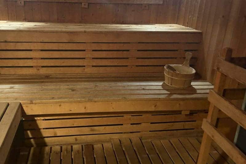 Wooden sauna interior featuring double layered benches, with a wooden bucket in a traditional sauna setting.