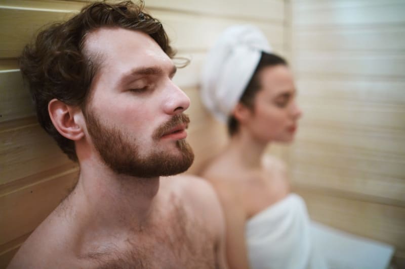 Couple relaxing together in a sauna, eyes closed, enjoying a shared moment of mindfulness and relaxation.