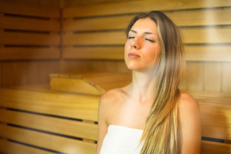 Woman experiencing deep relaxation through meditation in a sauna, eyes closed and serene.