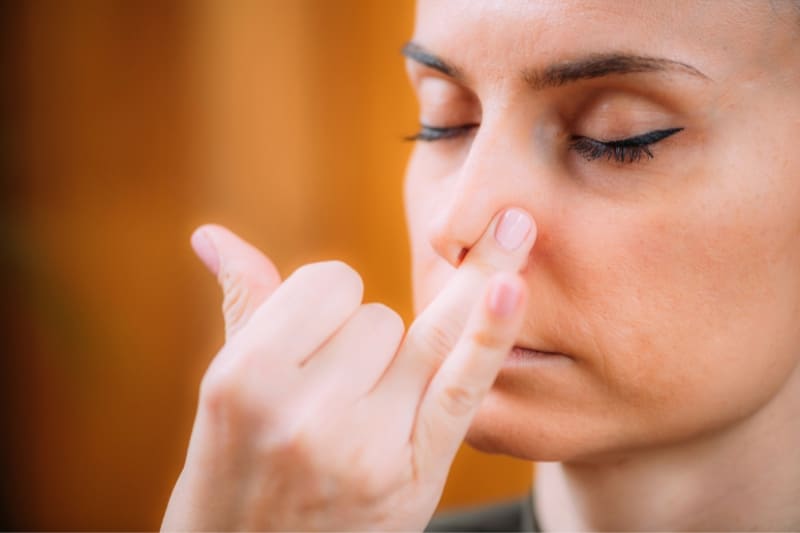 Woman performing a breathing exercise (pranayama) in a sauna, focusing on deep inhalation for relaxation.