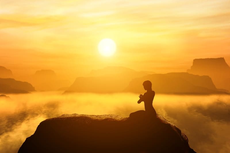 Individual meditating at sunrise on a mountaintop, embracing the early morning calm and golden light.