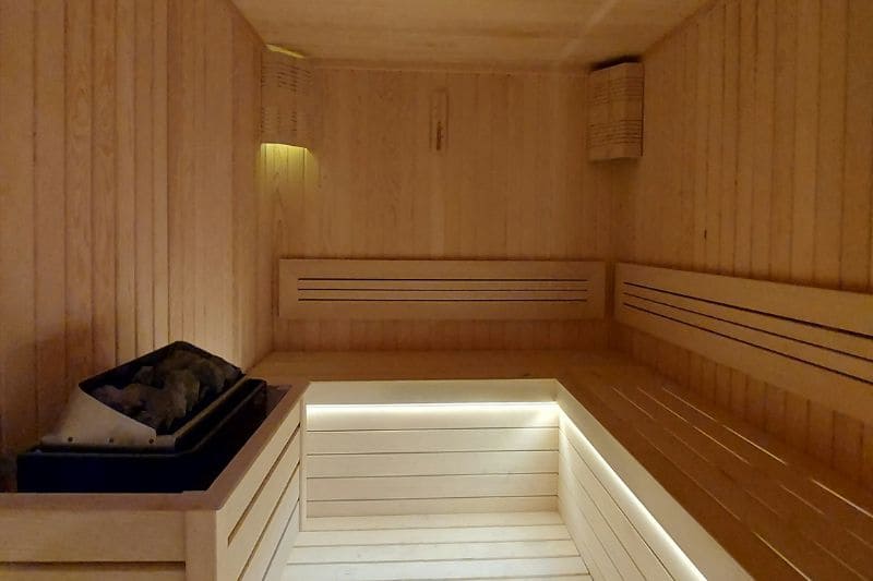 A minimalist sauna with light wood interior, featuring built-in lights and a modern heater.