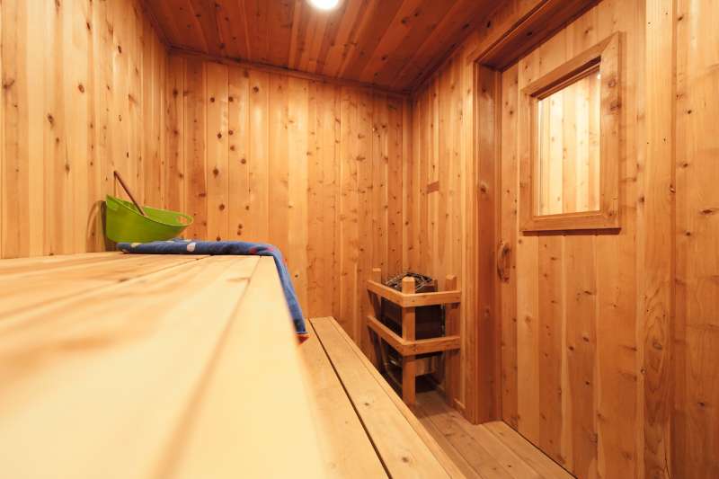 A simple wooden sauna with a small window, featuring a wooden bench and a traditional heater.