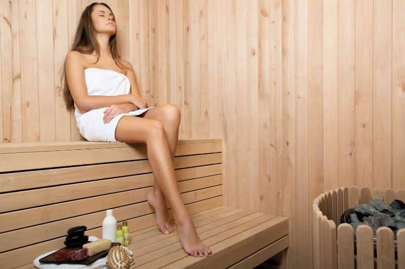 A woman sitting and relaxing in a traditional sauna, enjoying the heat therapy in a wooden sauna room.