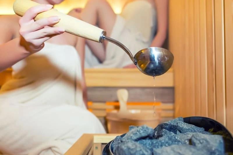 Close-up of a woman's hand pouring water on sauna rocks using a ladle.