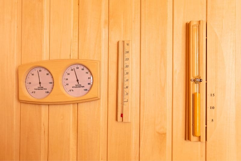 Analog sauna thermometers mounted on a wooden panel, ideal for tracking temperature in a traditional sauna setting.