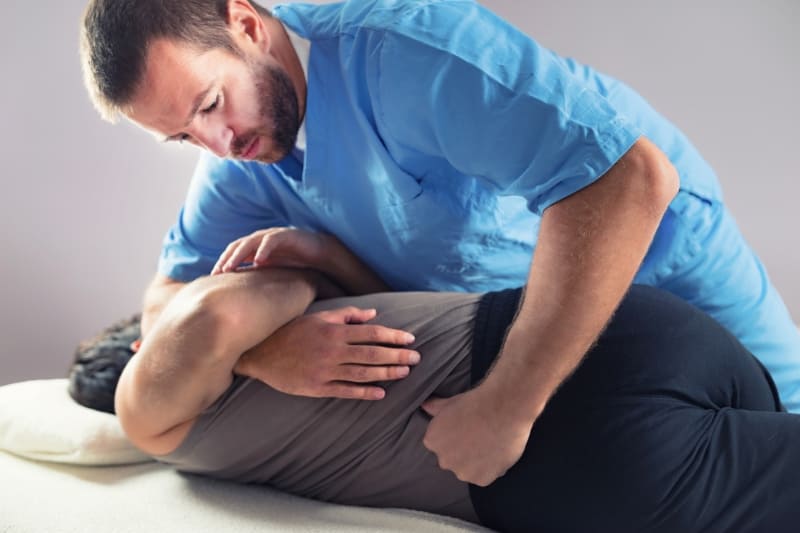 A chiropractor in a blue uniform adjusting a patient's back for pain relief on a treatment table.