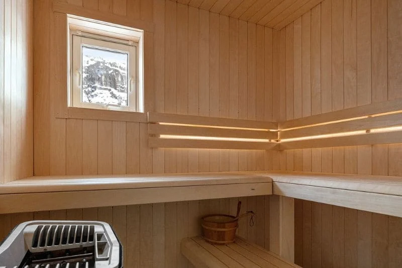 Compact sauna with light wood interior, a small window, and a corner-mounted sauna heater.