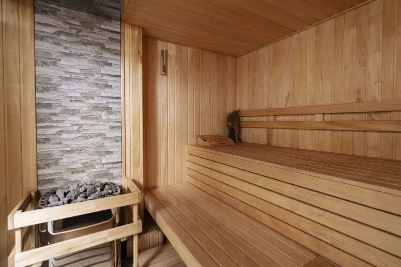 Traditional sauna featuring wooden benches and a stone-clad sauna heater for an authentic experience.