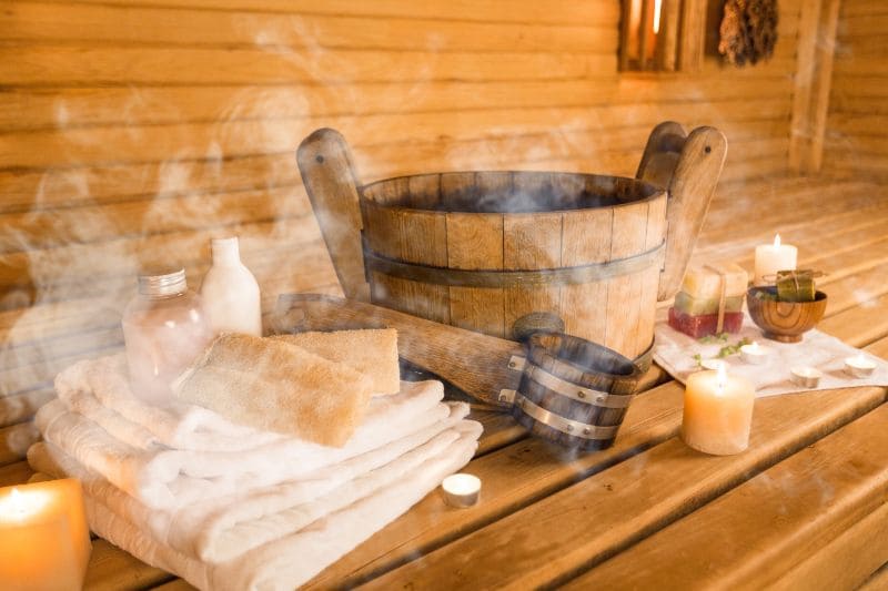 Steaming wooden bucket and ladle, fluffy towels, and aromatherapy oils create a relaxing ambiance in a traditional sauna.