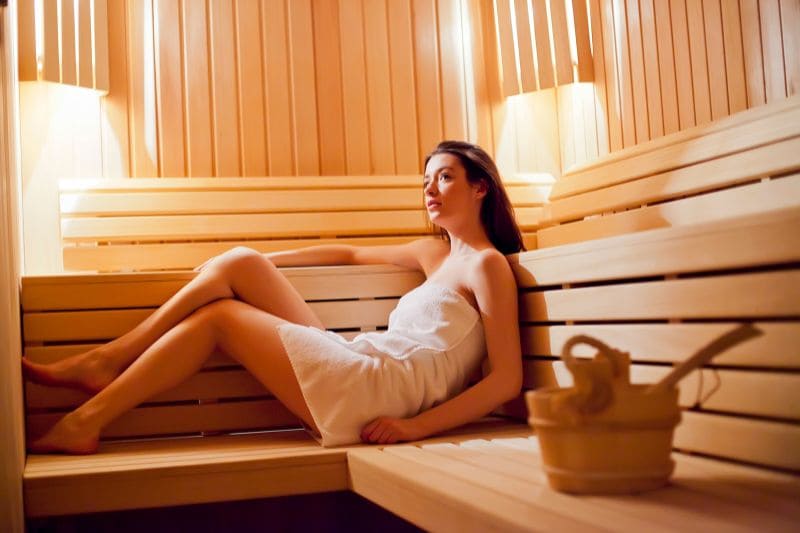 A woman relaxes and enjoys the warmth of a traditional sauna, promoting wellness and detoxification.