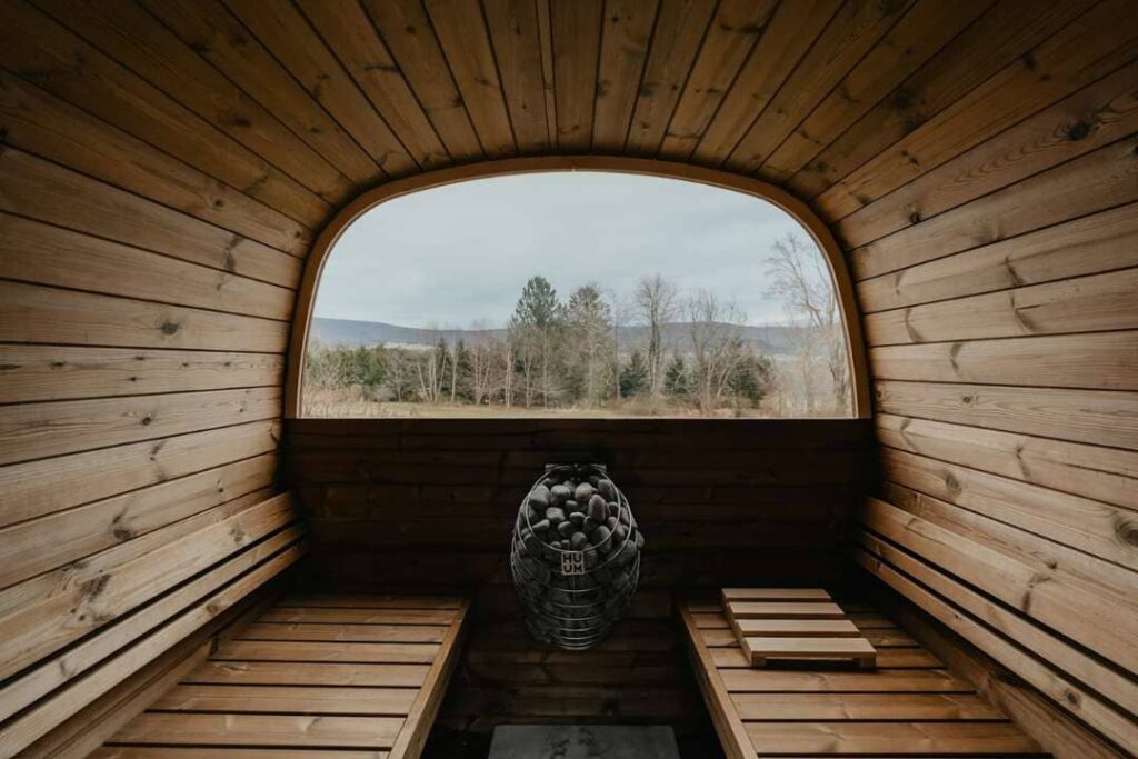 Barrel sauna design featuring panoramic arched window with forest view and centrally placed sauna heater