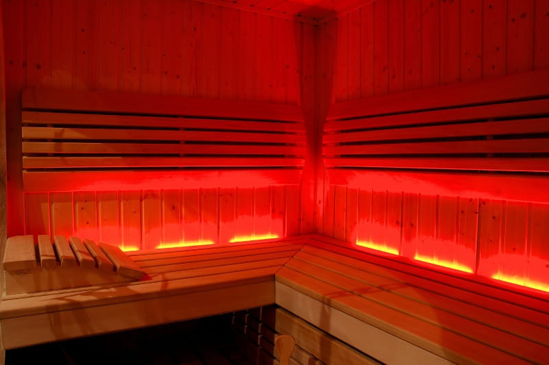 A wooden sauna illuminated with red chromotherapy lights, showcasing the calming and therapeutic effects of chromotherapy lights in saunas.