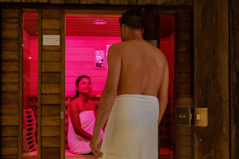 A couple relaxing in a sauna illuminated with pink chromotherapy light, illustrating the soothing ambiance created by chromotherapy lights in saunas