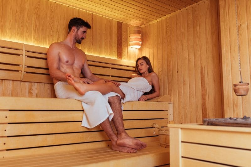 A couple relaxing in a sauna, wrapped in towels, enjoying the warmth.