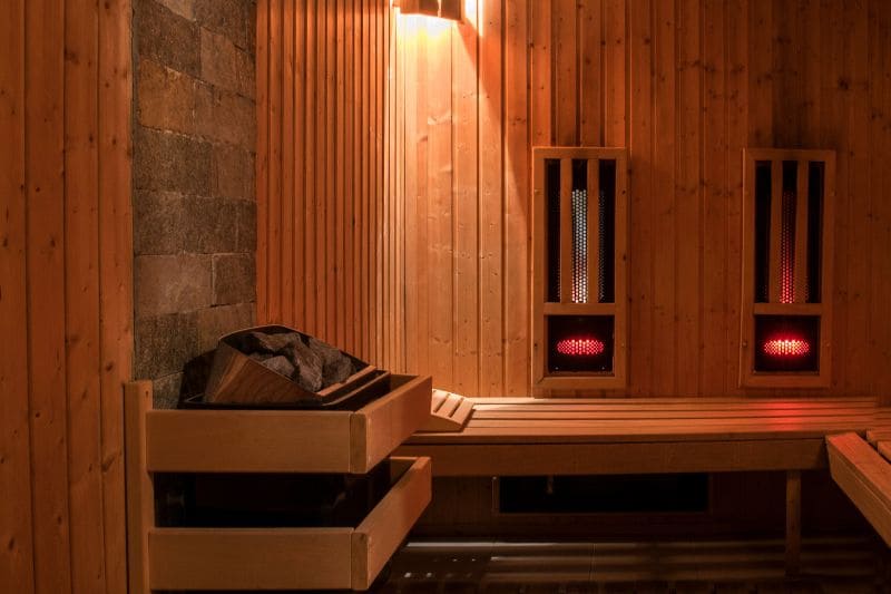 Empty hybrid sauna interior showing wooden benches, infrared sauna panels, and an electric heater, highlighting the cozy atmosphere.