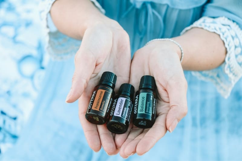 A woman holding three bottles of essential oils, potentially for use in aromatherapy or a sauna experience.