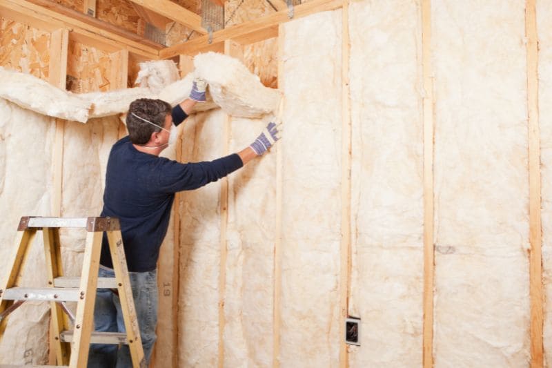 Worker insulating wall with fiberglass batts in wooden frame construction