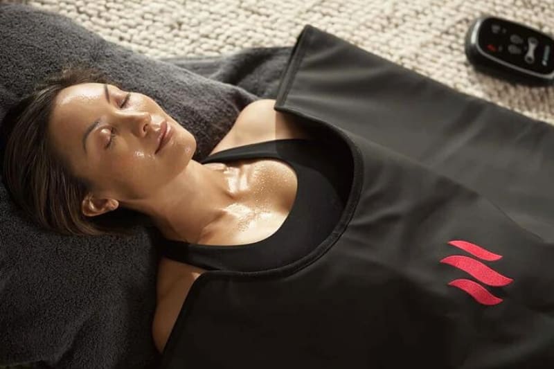 Woman experiencing relaxation and sweating inside the MiHigh Infrared Sauna Blanket during a wellness session.