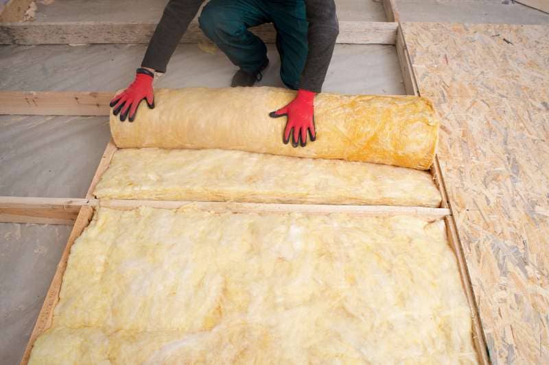 Worker rolling out mineral wool insulation for effective sauna insulation of the floor