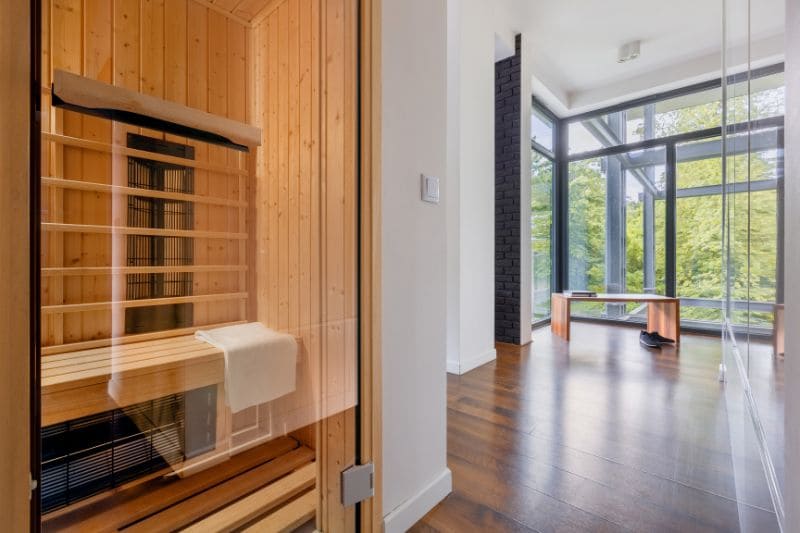 A modern infrared sauna with a glass front, situated in a contemporary home with large windows and hardwood floors.