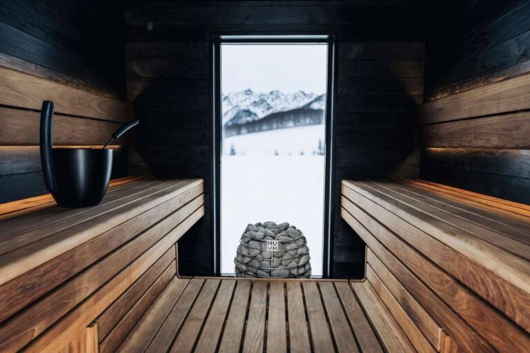 Modern sauna design with large window overlooking snowy mountains, featuring wooden benches and a "Huum" sauna heater