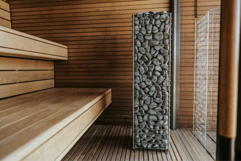 Modern sauna interior featuring wooden benches and a stone-filled heater column