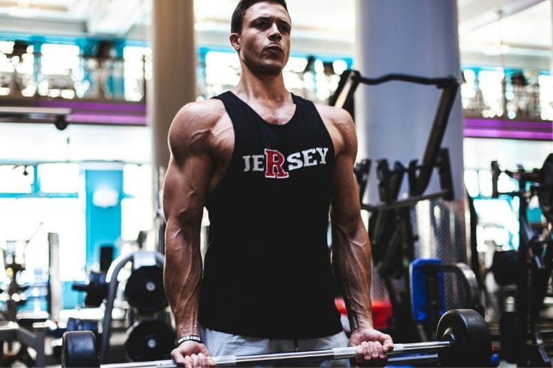 A muscular man lifts weights in a gym, emphasizing the role of strength training in achieving fitness goals