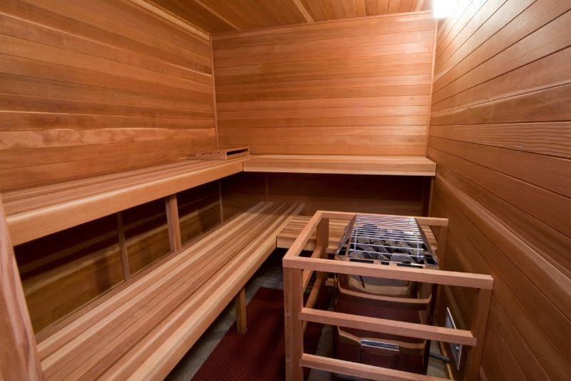 Interior of a sauna with cedar wood paneling and a modern electric sauna heater.