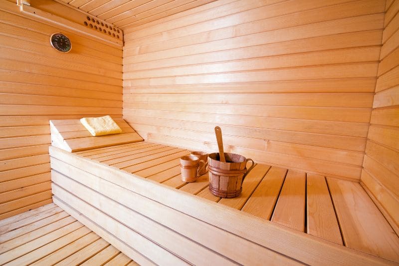 A small sauna with a wooden bench, ladle, bucket, and cups.