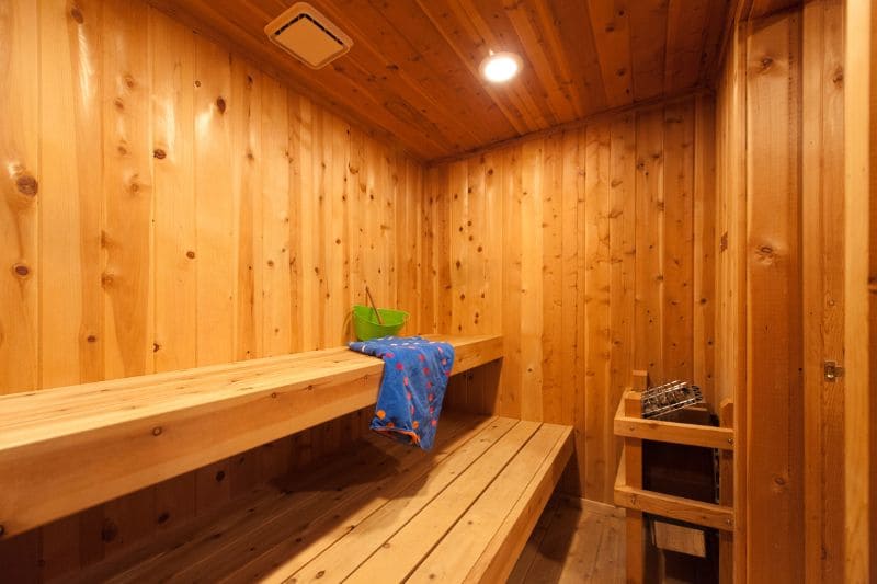 A traditional sauna interior with wooden walls and benches. The sauna features a bucket of water and a towel on the top bench.