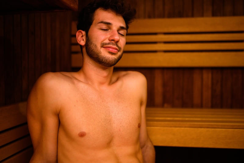 A man enjoying the heat in a sauna, eyes closed, soaking in the warmth.