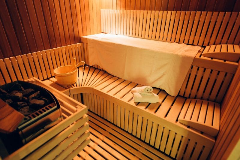 A close-up of a sauna stove with heated stones, a metal grate, and a wooden bucket. This image highlights the traditional heating system used in many saunas.