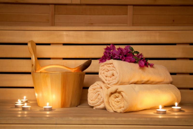 Rolled up towels, a wooden bucket, and candles create a serene and inviting atmosphere in a sauna.