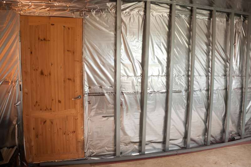 Sauna construction showing vapor barrier installation and wooden door, demonstrating proper moisture control techniques for sauna insulation