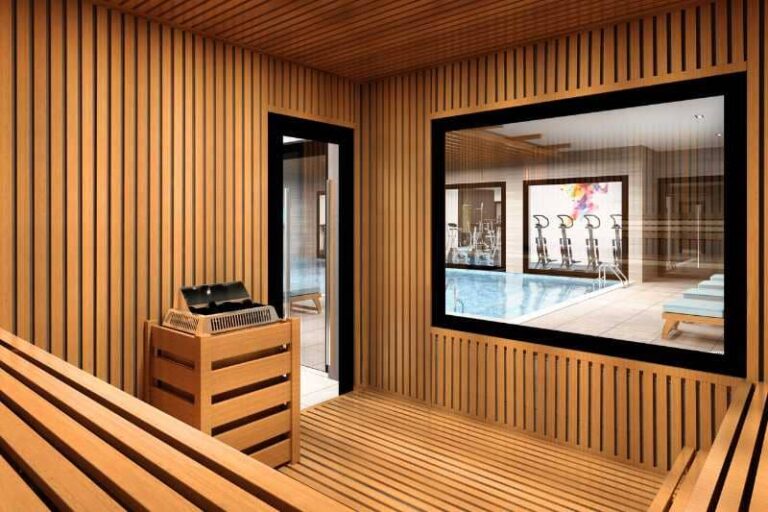 A sauna with a large window overlooking a swimming pool and gym area.