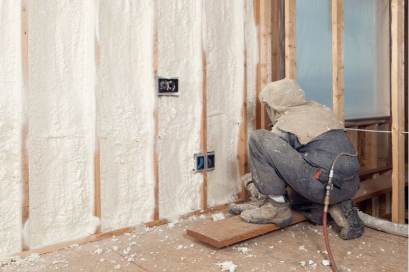 Contractor applying spray foam insulation between wall studs