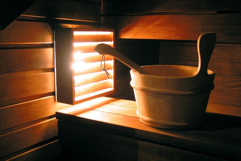 A wooden bucket and ladle in a steam room with the light illuminating the steam.