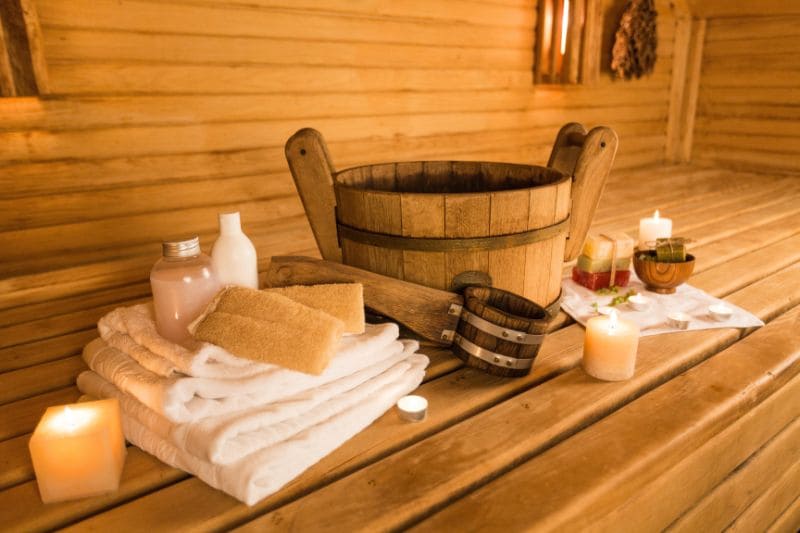 Traditional wooden sauna with neatly arranged towels, a wooden bucket, candles, and spa accessories creating a warm, inviting decor.