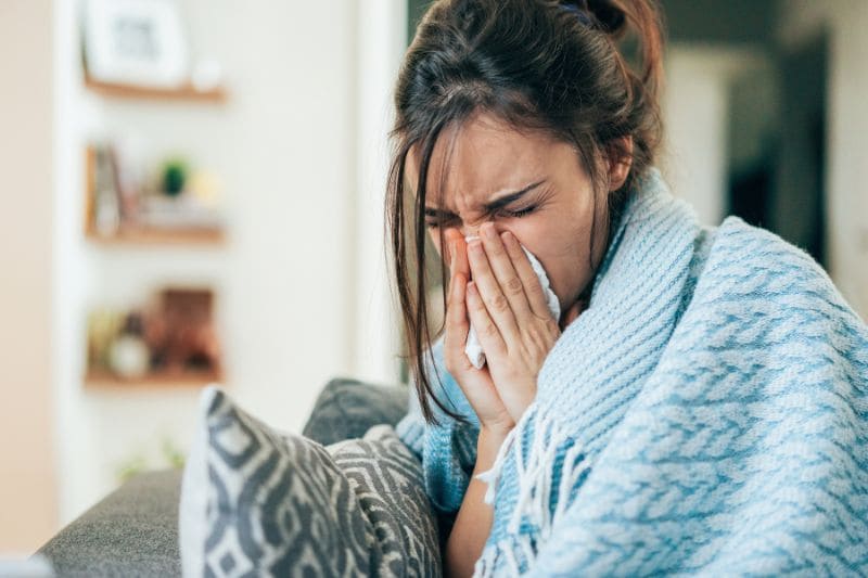 A woman wrapped in a blanket, sneezing, and suffering from a cold.