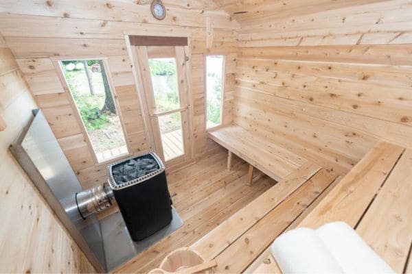 Interior view of the Dundalk CT Georgian Cabin 6 Person Sauna with bench seating, windows, and an electric heater, showcasing the sauna's spacious design and natural light.