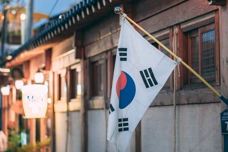 South Korean flag displayed outside a traditional Korean building with wooden architecture and lanterns visible in the background