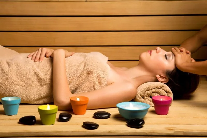 Woman enjoying a massage in sauna, surrounded by aromatherapy candles and hot stones