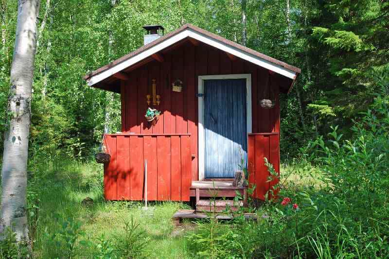 Rustic red Finnish sauna cabin nestled in a lush green forest setting