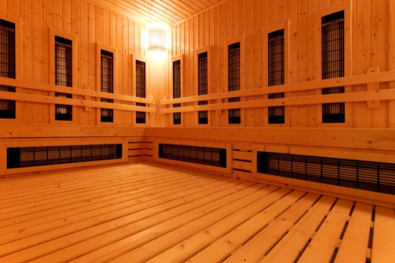 The interior of a spacious full spectrum infrared sauna, featuring wooden benches and strategically placed heaters for even heat distribution.