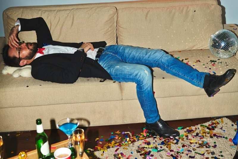 Man passed out on couch after party, surrounded by drinks and confetti