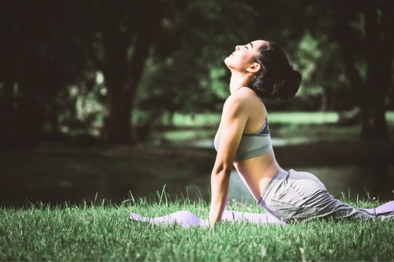 Woman performing cobra pose yoga stretch on grass in peaceful outdoor nature setting