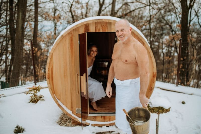 Couple enjoying in a barrel sauna in the morning surrounded by snowy woods